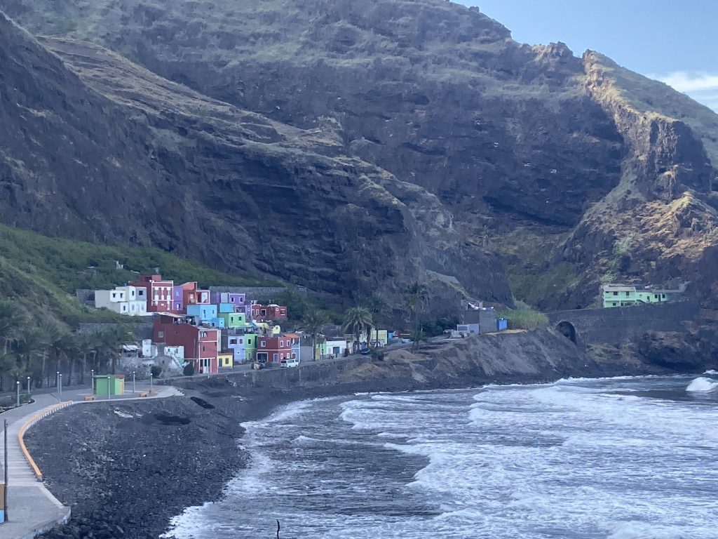 Baai met rechts hoge grijze rots en gekleurde huisjes aan de voet ervan.