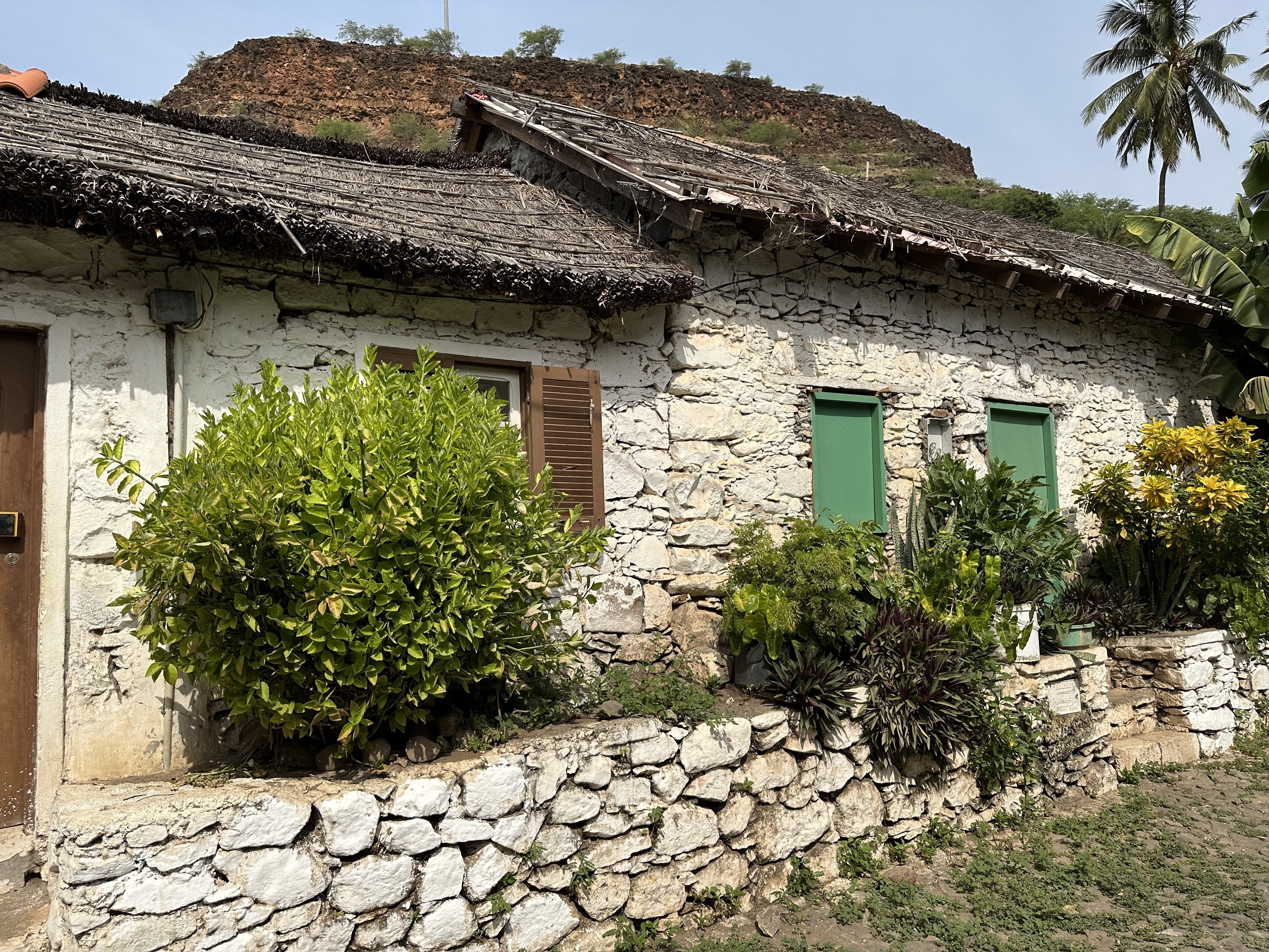 Oud, wit-grijs huis met rieten dak en groene luiken in Cidade Velha.