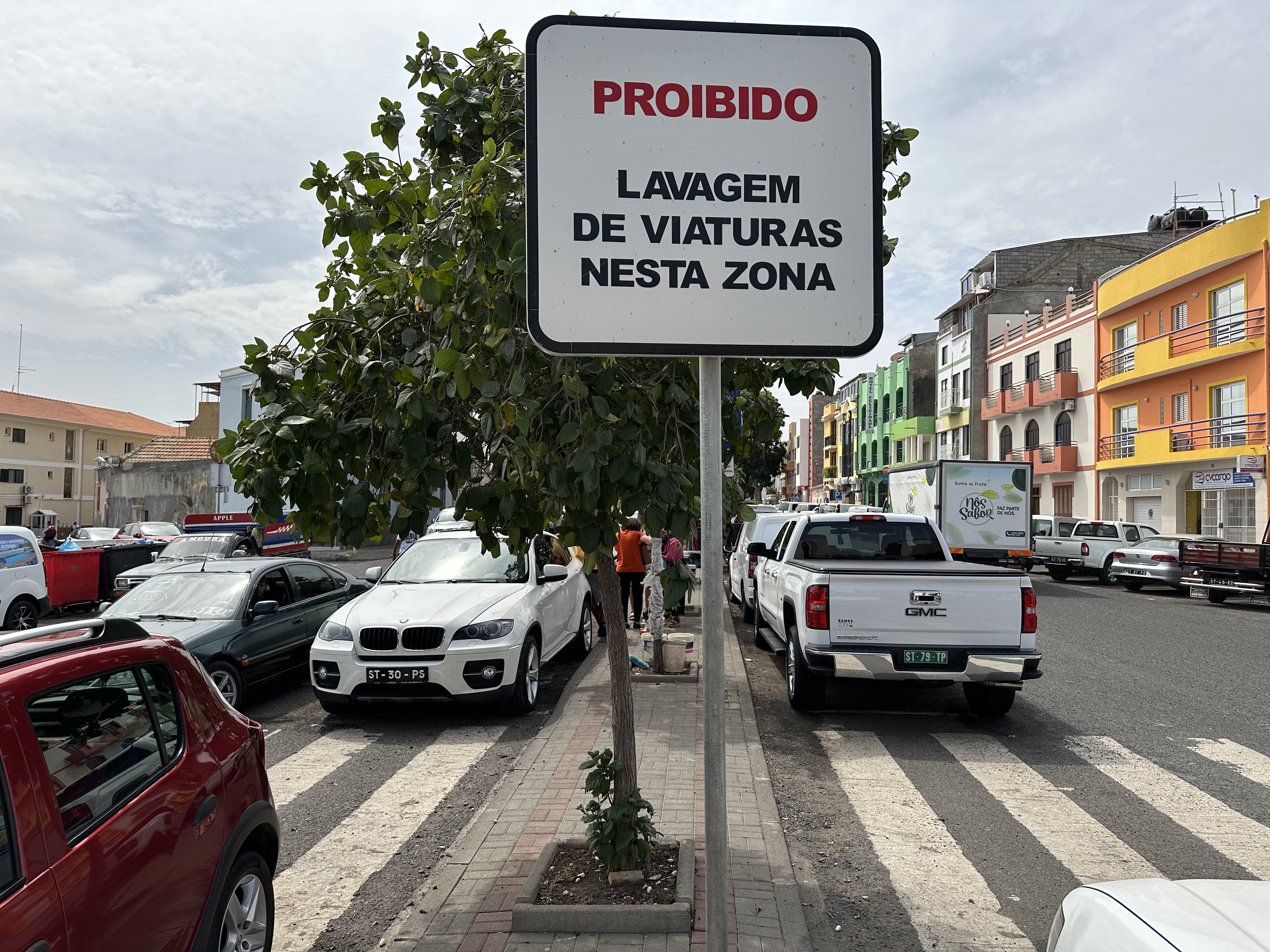 Personen wassen auto's achter bord met: "Verboden auto's te wassen in het Portugees".