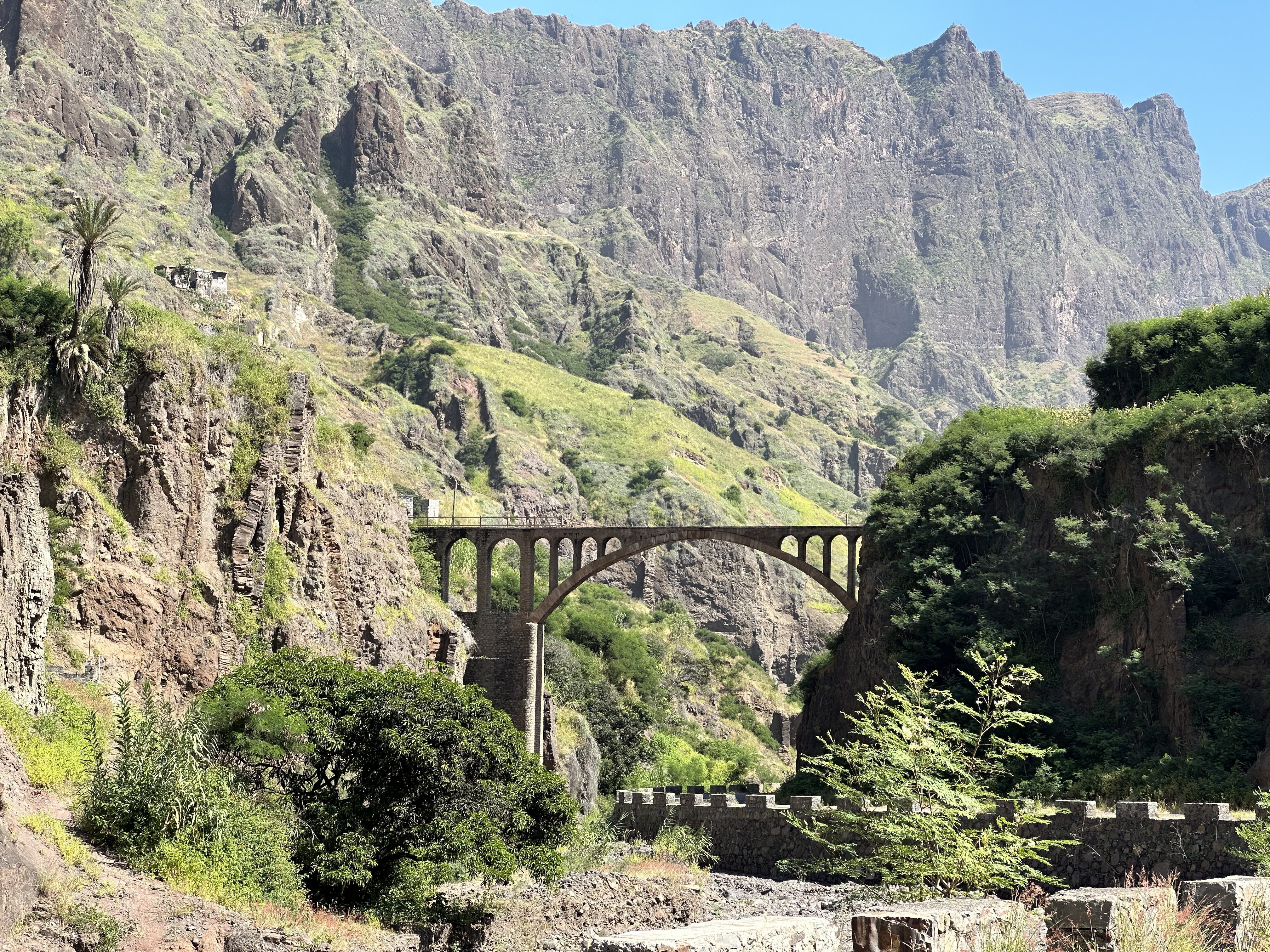 Boogbrug tussen heel hoge, groene rotsen.